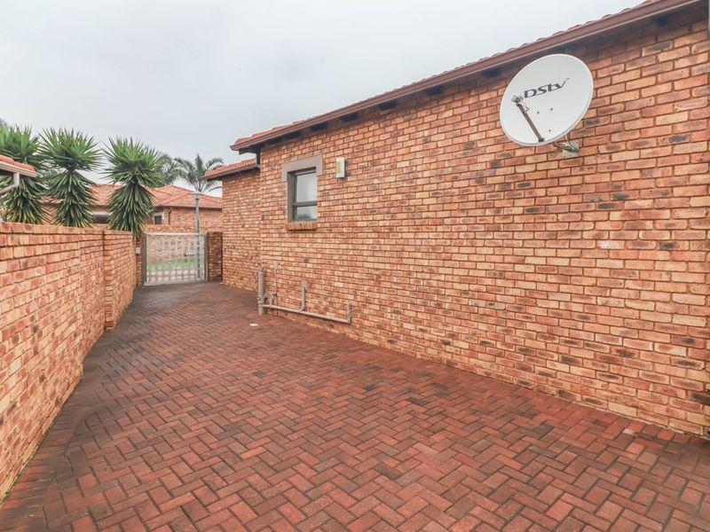 A side view of the property featuring face brick exterior walls, a paved walkway, and a secure metal gate leading to the rear garden area.