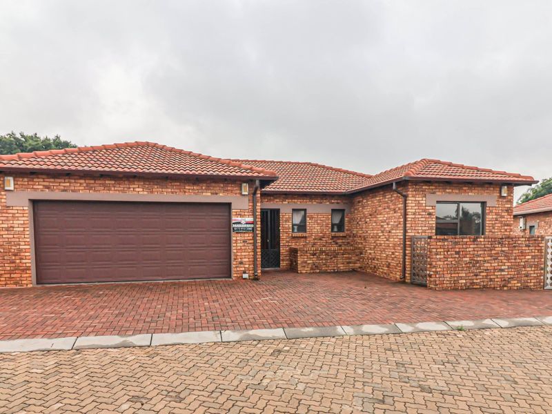 Front elevation of a face-brick cluster home featuring a double garage, paved driveway, and secure entrance.