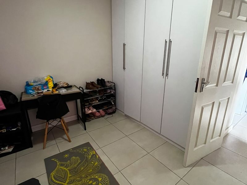 A bedroom featuring neutral tiled flooring, white built-in cupboards with modern handles, and classic ceiling cornicing.