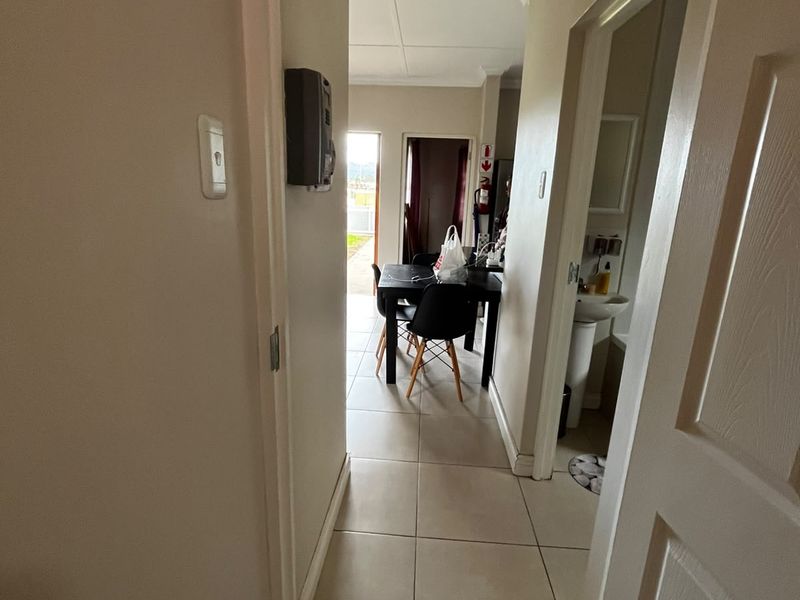 A view through a hallway leading to an open plan living area, with a glimpse of an adjacent bathroom featuring a pedestal basin.