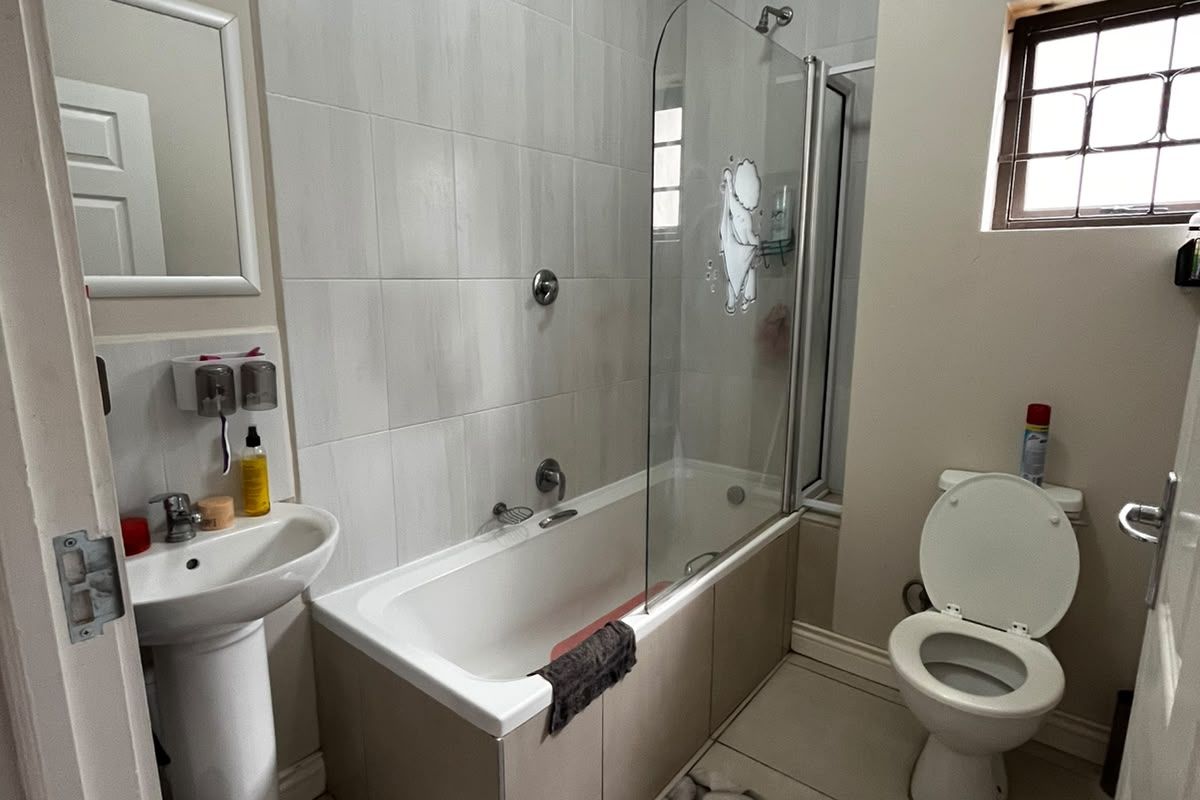 A functional bathroom featuring a pedestal basin, a bathtub with a glass shower screen, and a toilet, finished with neutral wall and floor tiles.