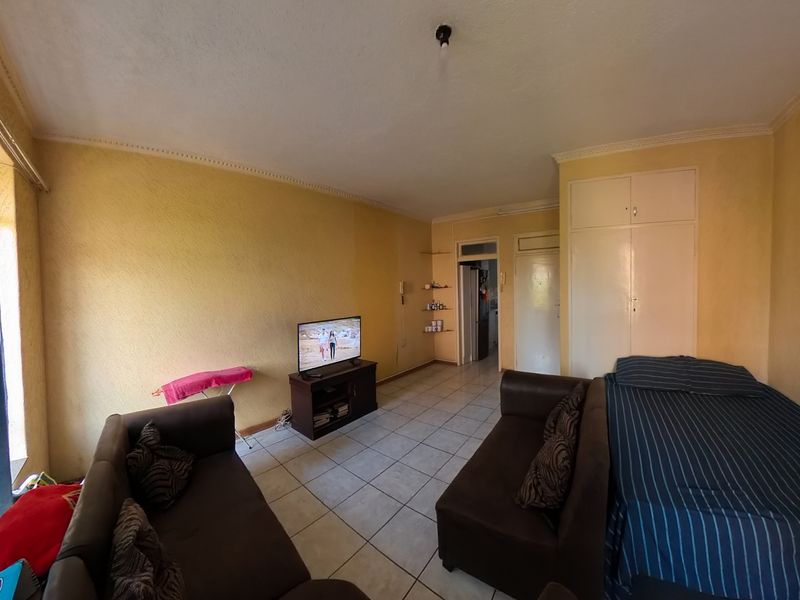 A bedroom featuring built-in cupboards, tiled flooring, and cornice detailing, offering a functional space with potential for cosmetic updates.