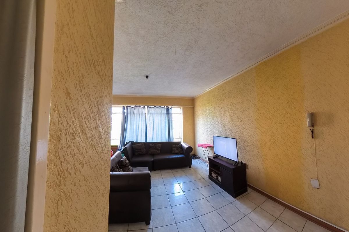 A living room featuring tiled flooring, textured yellow walls, and ceiling cornice detailing, offering a functional space with natural light from the window.