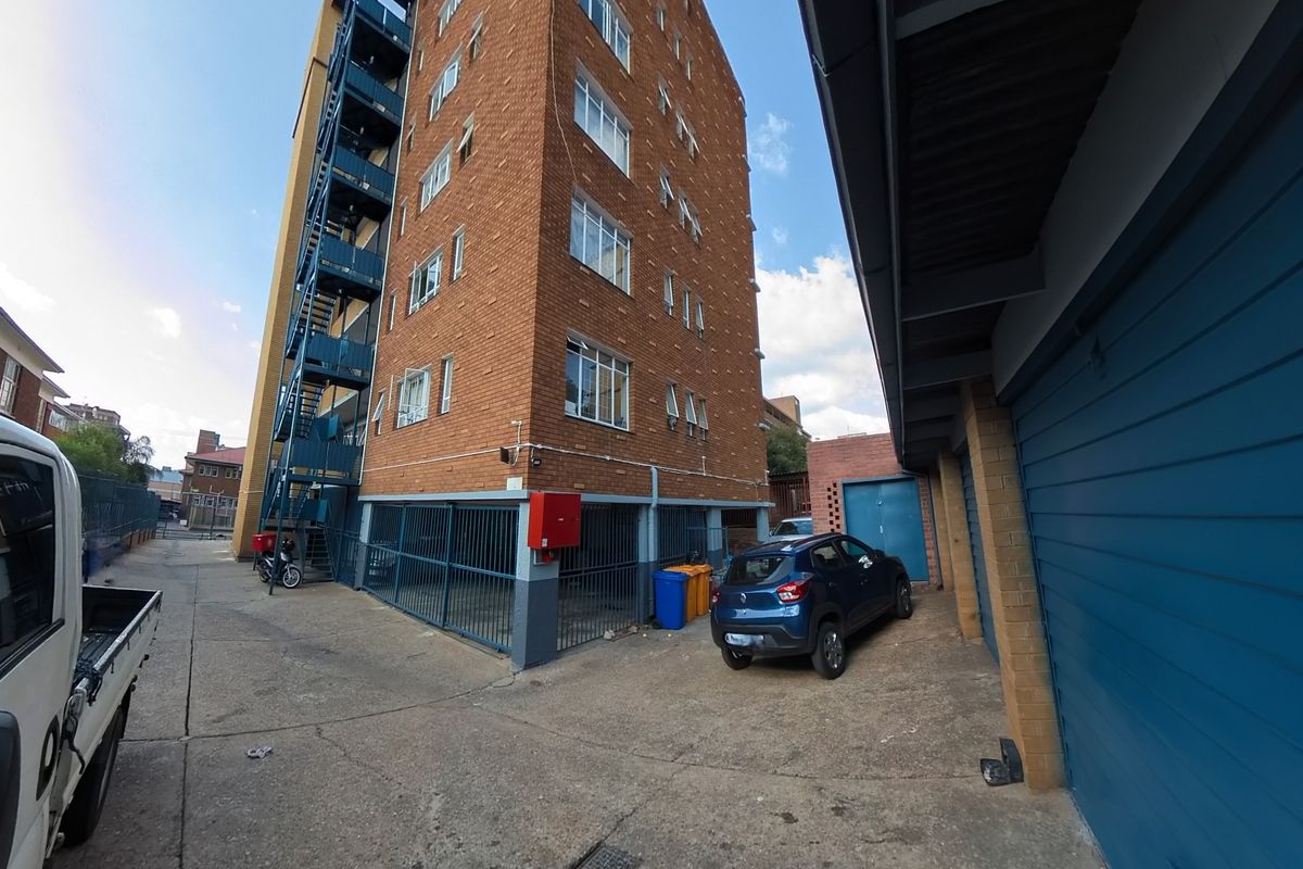 Rear view of a multi-story brick apartment building featuring an external fire escape staircase and ground-level garage access.
