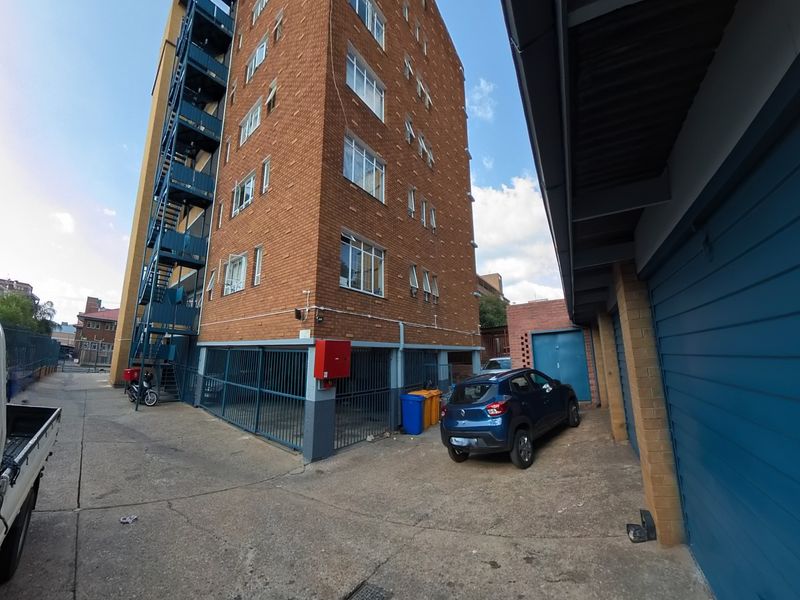Rear view of a multi-story brick apartment building featuring an external fire escape staircase and ground-level garage access.