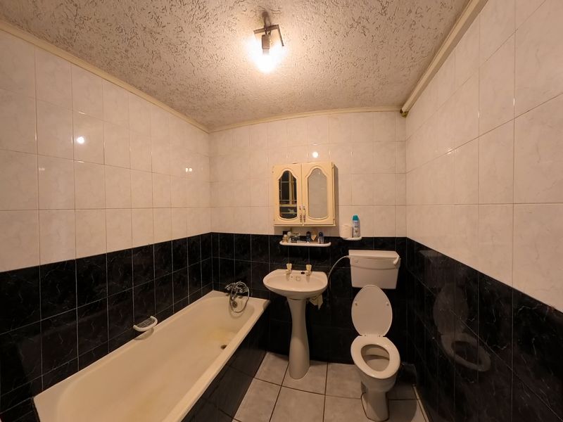 A dated bathroom featuring a pedestal sink, toilet, and bathtub with two-tone wall tiling and tiled flooring.