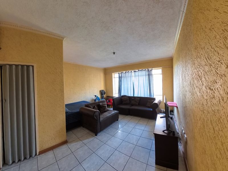 A living room featuring textured yellow walls, ceramic floor tiling, and a folding door, offering a dated aesthetic ready for modernization.