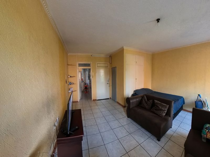 Open-plan living area featuring tiled flooring, built-in storage cupboards, and decorative cornicing, offering a functional layout with potential for cosmetic updates.