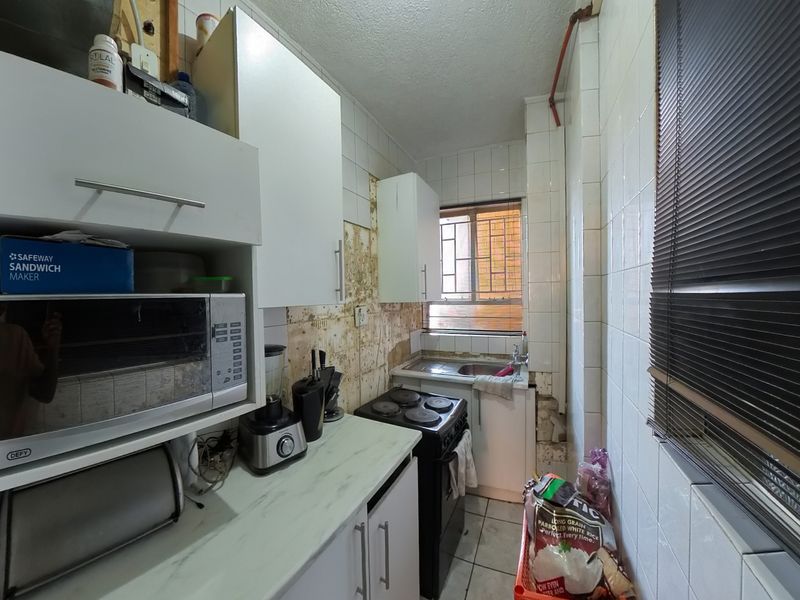 A compact kitchen featuring white cabinetry, a stainless steel sink, and an electric stove, currently requiring significant wall repairs and tile restoration.