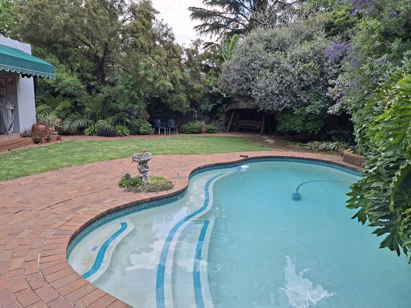 A well-maintained backyard featuring a swimming pool with brick paving, a lush lawn, and mature garden landscaping.