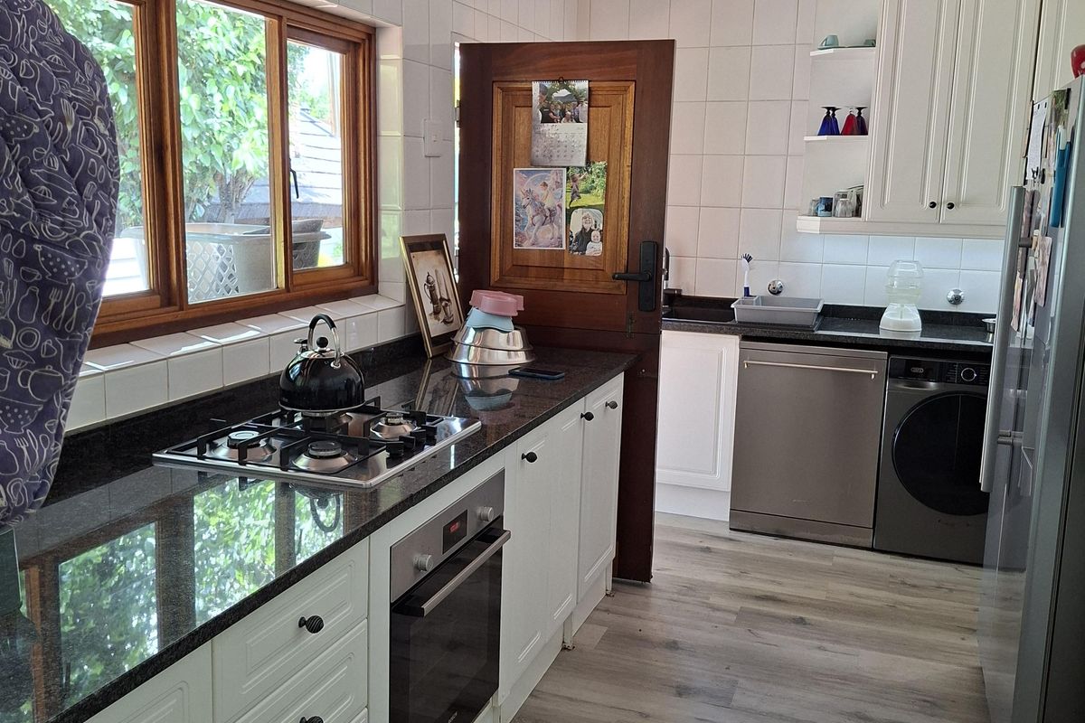 A functional kitchen featuring granite countertops, white cabinetry, a built-in oven, gas hob, and modern laminate flooring with ample natural light.