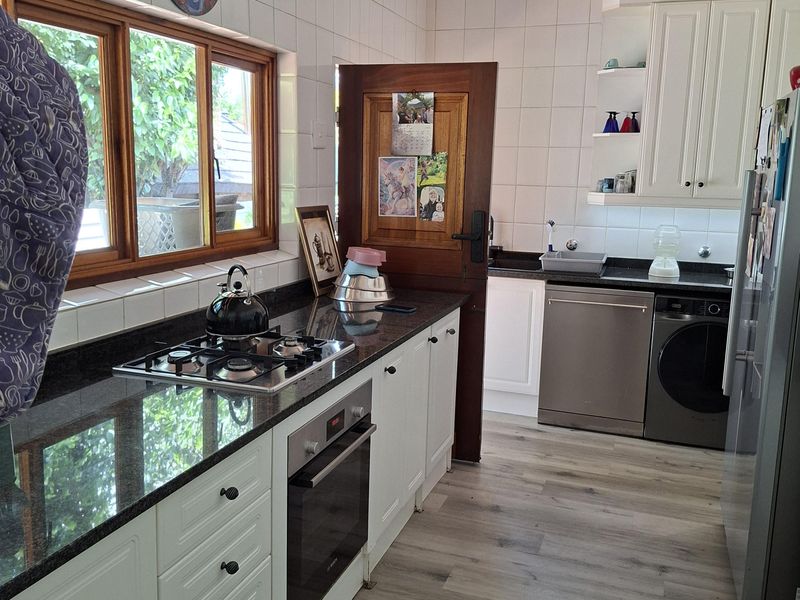 A functional kitchen featuring granite countertops, white cabinetry, a built-in oven, gas hob, and modern laminate flooring with ample natural light.