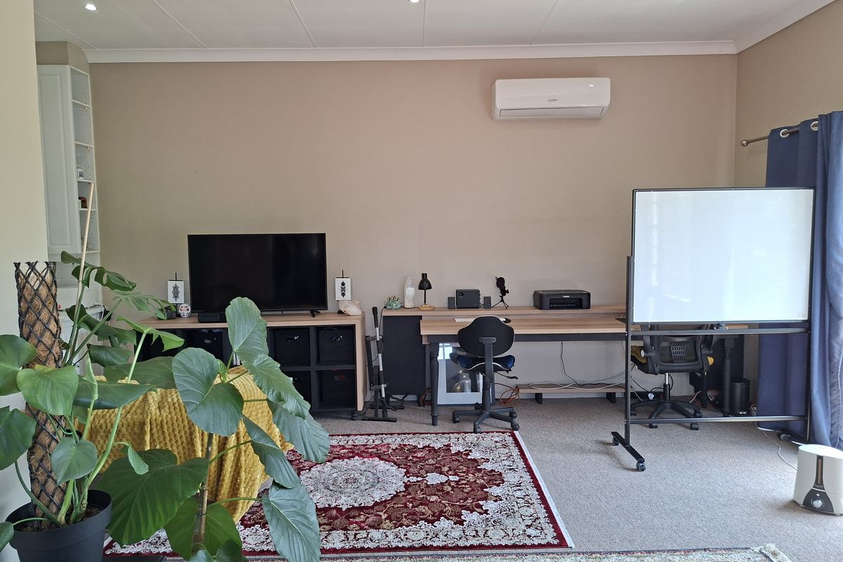 A functional living area featuring a split-system air conditioner, recessed downlighting, and built-in shelving, currently utilized as a multi-purpose workspace.