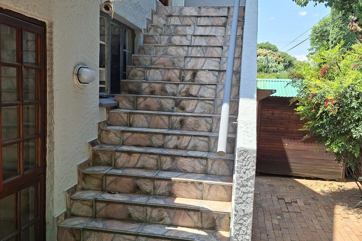 Exterior rear view featuring a tiled staircase with a metal handrail leading to an elevated entrance, set against a paved garden area.