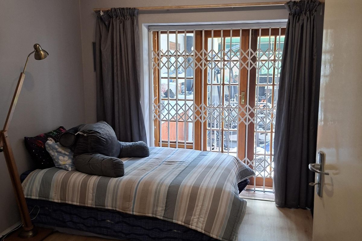 A bedroom featuring laminate flooring, a sliding glass door with a security gate, and neutral wall tones.