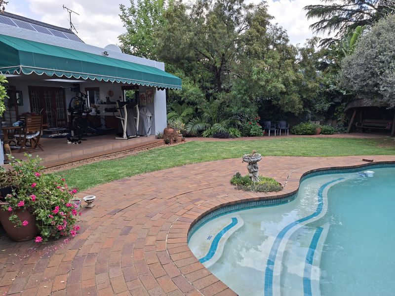 Outdoor pool area featuring a swimming pool, brick paved surround, and a covered patio with a retractable awning.