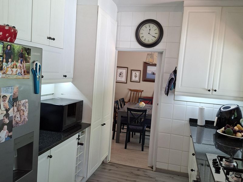 A functional kitchen featuring white cabinetry, dark granite countertops, a gas hob, and modern laminate flooring, with a direct view into the dining area.