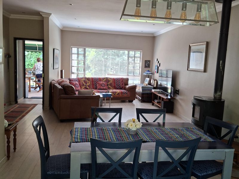 Spacious open-plan living and dining area featuring laminate flooring, a wood-burning fireplace, and modern pendant lighting, with direct access to an outdoor patio.