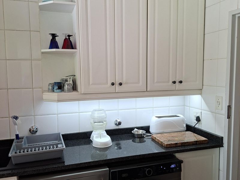 A functional scullery area featuring white cabinetry, dark granite countertops, tiled backsplash, and integrated laundry and dishwashing appliances.