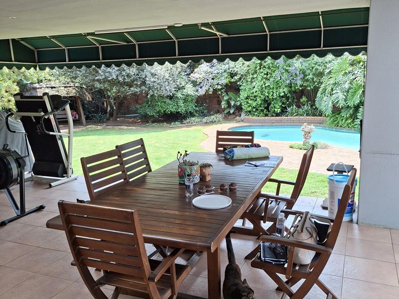 Covered outdoor patio area featuring tiled flooring and a retractable awning, overlooking a garden and swimming pool.