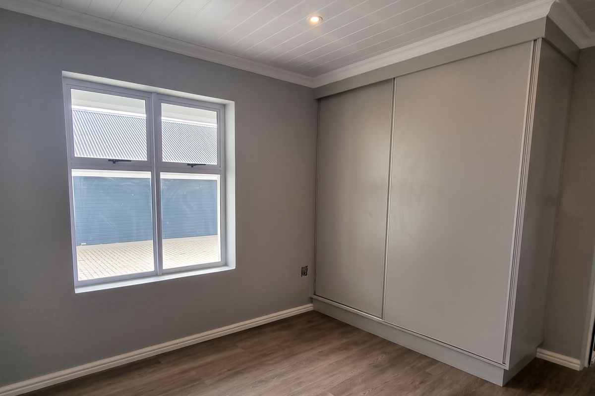 A bright, empty bedroom featuring modern laminate flooring, a built-in sliding wardrobe, and a clean tongue and groove ceiling with recessed lighting.