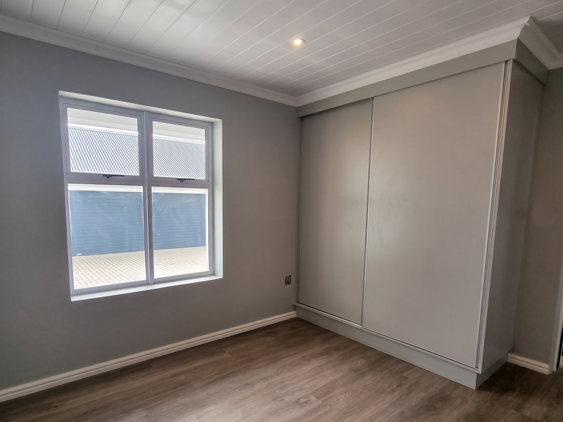 A bright, empty bedroom featuring modern laminate flooring, a built-in sliding wardrobe, and a clean tongue and groove ceiling with recessed lighting.