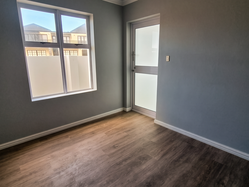 A bright, empty bedroom featuring modern laminate flooring, a tongue and groove ceiling, and a frosted glass door leading to the exterior.