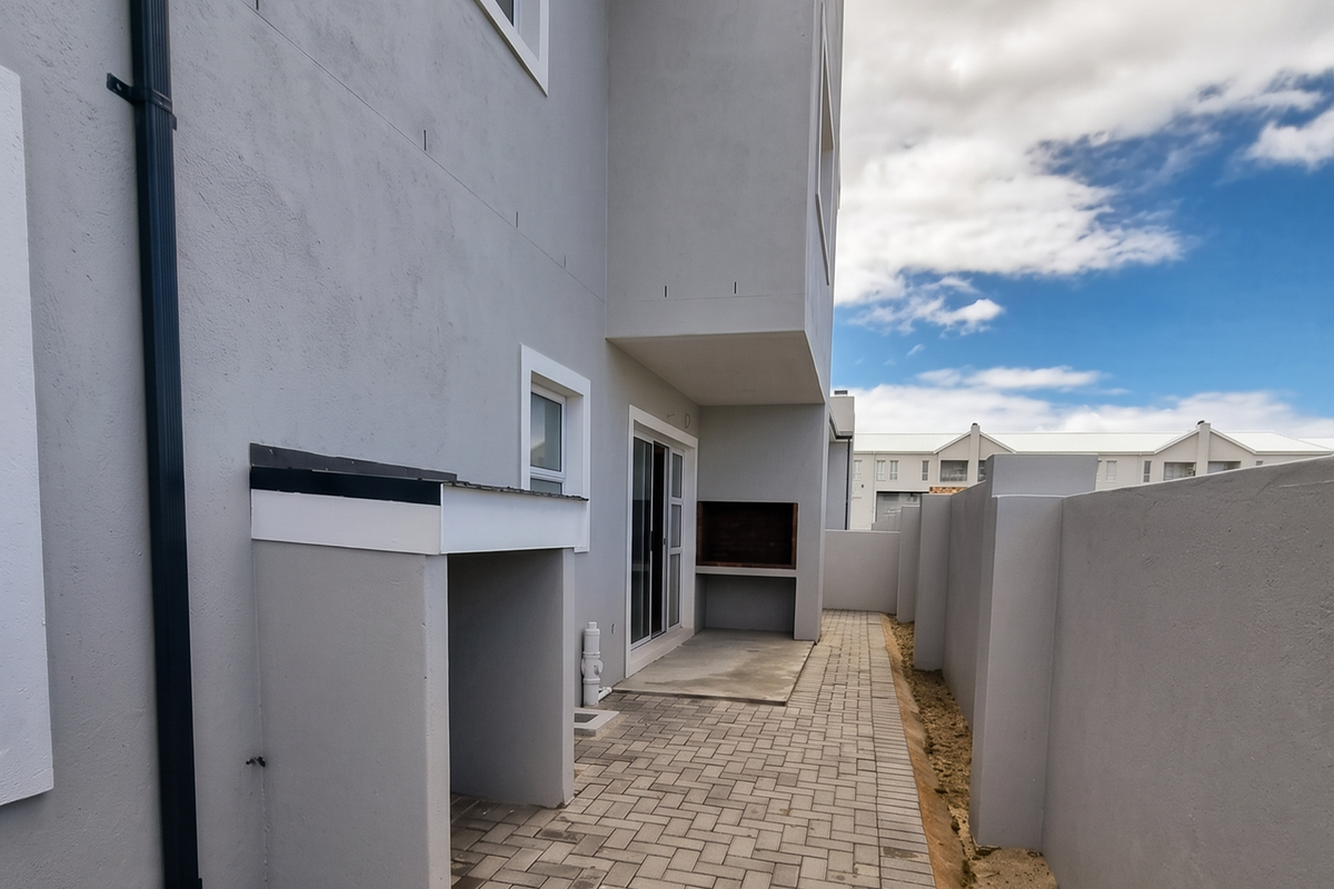 A clean, paved rear patio area featuring a built-in braai, sliding door access, and secure boundary walls.