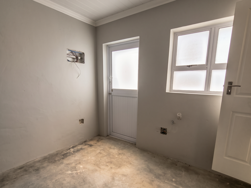 An empty, unfinished utility or laundry room featuring exposed electrical wiring, plumbing connections, a concrete floor, and a frosted glass exterior door.