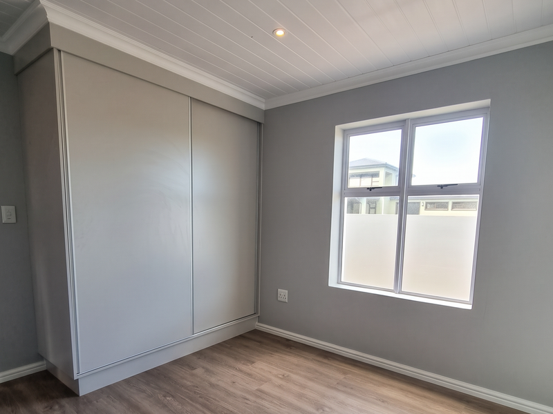 A bright, empty bedroom featuring modern laminate flooring, a built-in wardrobe, and a stylish tongue and groove ceiling with recessed lighting.
