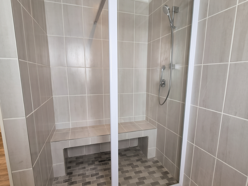 Modern walk-in shower featuring a built-in tiled bench, glass enclosure, handheld shower head, and neutral ceramic wall and floor tiling.