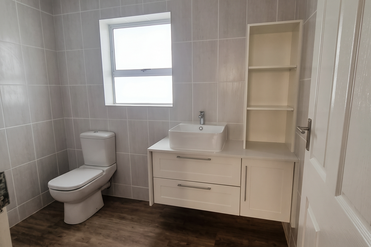 A clean, modern bathroom featuring a wall-mounted vanity with a vessel sink, built-in shelving, tiled walls, and wood-look flooring.