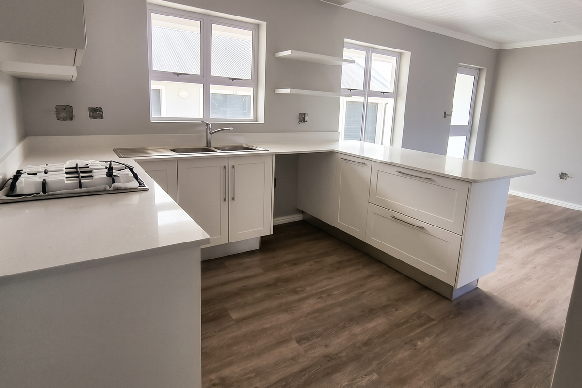 Modern kitchen featuring white cabinetry, stone countertops, gas hob, and wood-look laminate flooring in an open-plan layout.