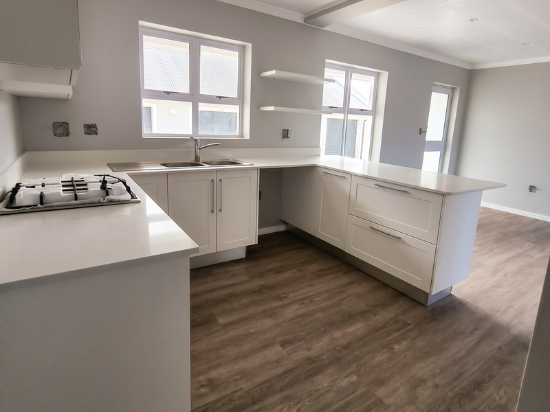 Modern kitchen featuring white cabinetry, stone countertops, gas hob, and wood-look laminate flooring in an open-plan layout.