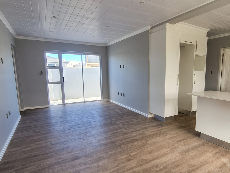 Spacious open-plan living area featuring modern laminate flooring, a tongue and groove ceiling with recessed lighting, and a sleek kitchen with built-in cabinetry.