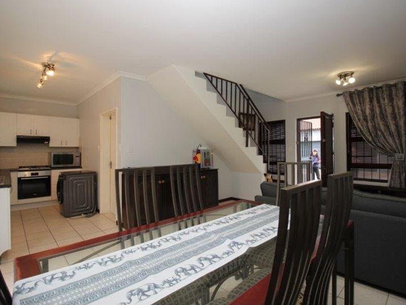 Open-plan living and dining area featuring a functional kitchen with built-in appliances, tiled flooring, and direct access to the exterior via a security gate.
