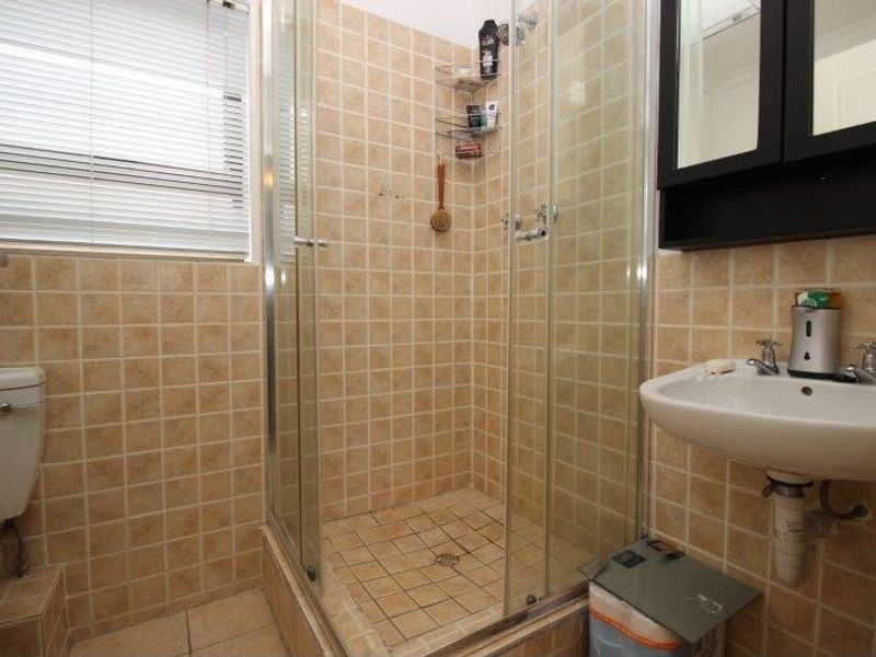 A compact bathroom featuring a shower enclosure, wall-mounted basin, and toilet with dated beige wall and floor tiling.