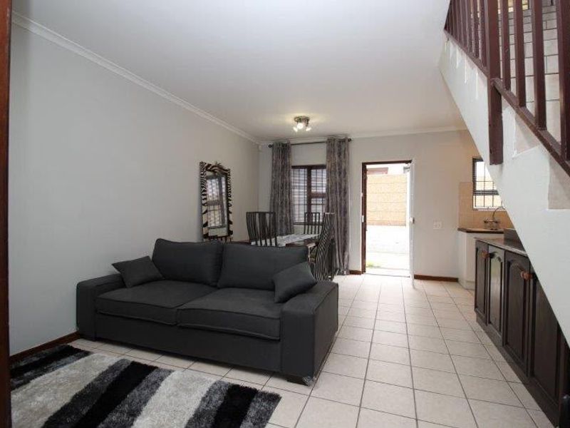 Open-plan living and dining area featuring tiled flooring, a staircase with a wooden balustrade, and direct access to the rear exterior.