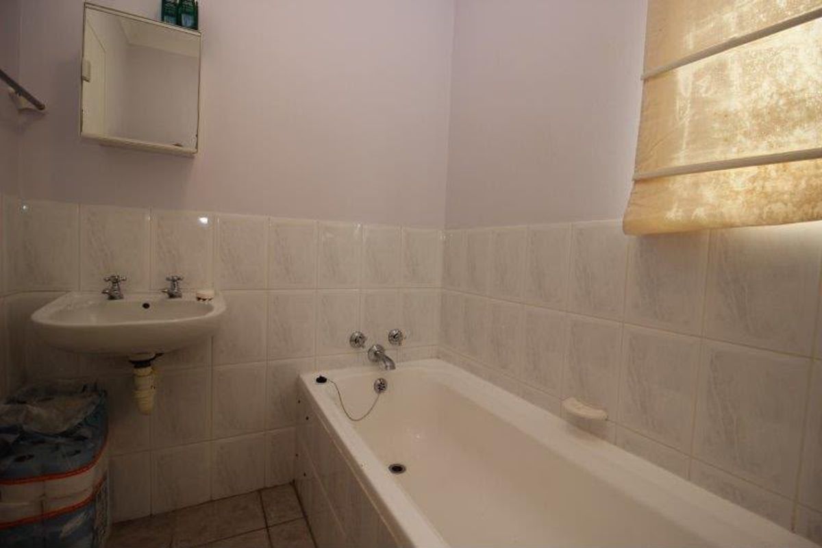 A functional bathroom featuring a built-in bathtub, wall-mounted basin, and tiled splashback, offering a blank canvas for modern renovation.