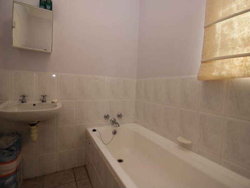 A functional bathroom featuring a built-in bathtub, wall-mounted basin, and tiled splashback, offering a blank canvas for modern renovation.