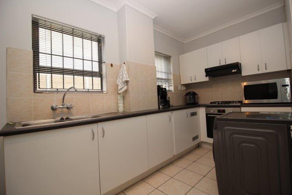 Functional kitchen featuring white cabinetry, dark countertops, built-in oven and hob, tiled splashbacks, and tiled flooring with security bars on the windows.
