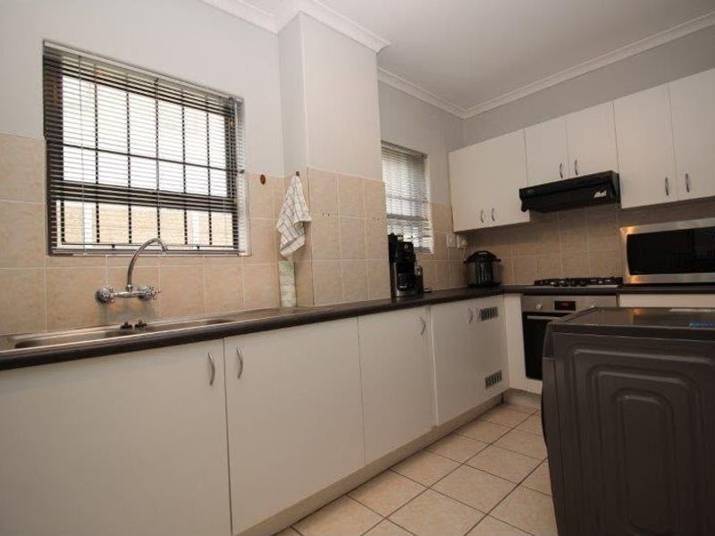 Functional kitchen featuring white cabinetry, dark countertops, built-in oven and hob, tiled splashbacks, and tiled flooring with security bars on the windows.