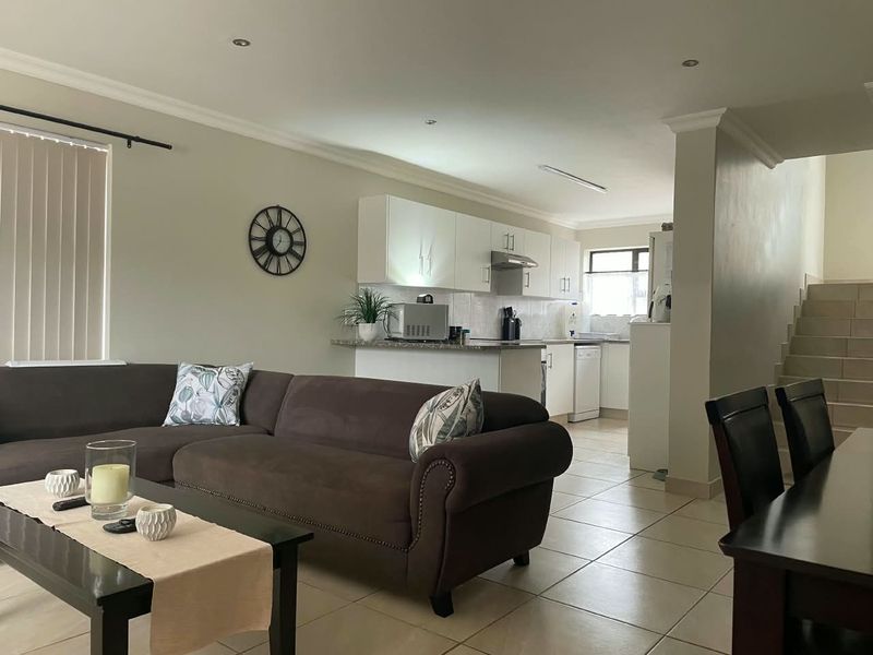 Open-plan living area featuring a kitchen with built-in cabinetry, tiled flooring throughout, and a staircase leading to the upper level.