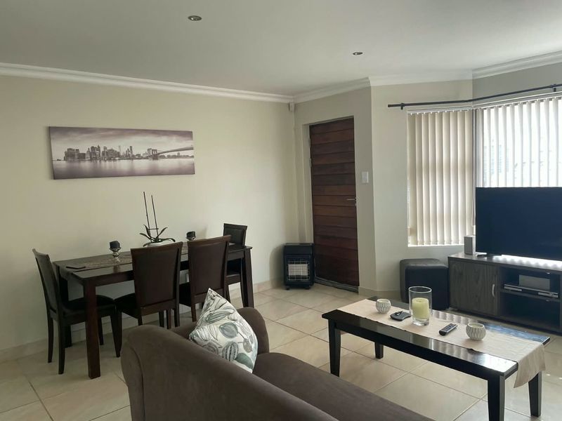 An open-plan living and dining area featuring tiled flooring, recessed downlights, and large windows with vertical blinds.