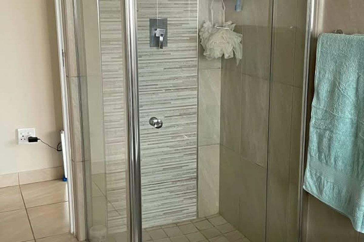 A functional bathroom featuring a glass-enclosed shower with modern tiled accents and a built-in bathtub, finished with neutral floor tiles.
