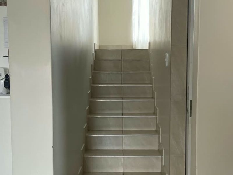 A clean, tiled hallway featuring a staircase leading to an upper level with neutral wall finishes.