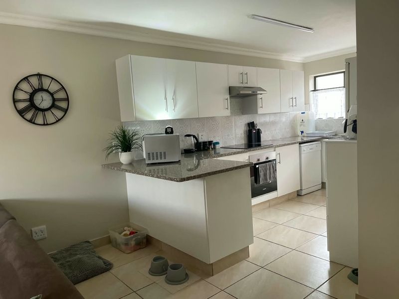 Open-plan kitchen featuring white cabinetry, granite countertops, built-in oven, and tiled flooring, seamlessly integrated with the living area.