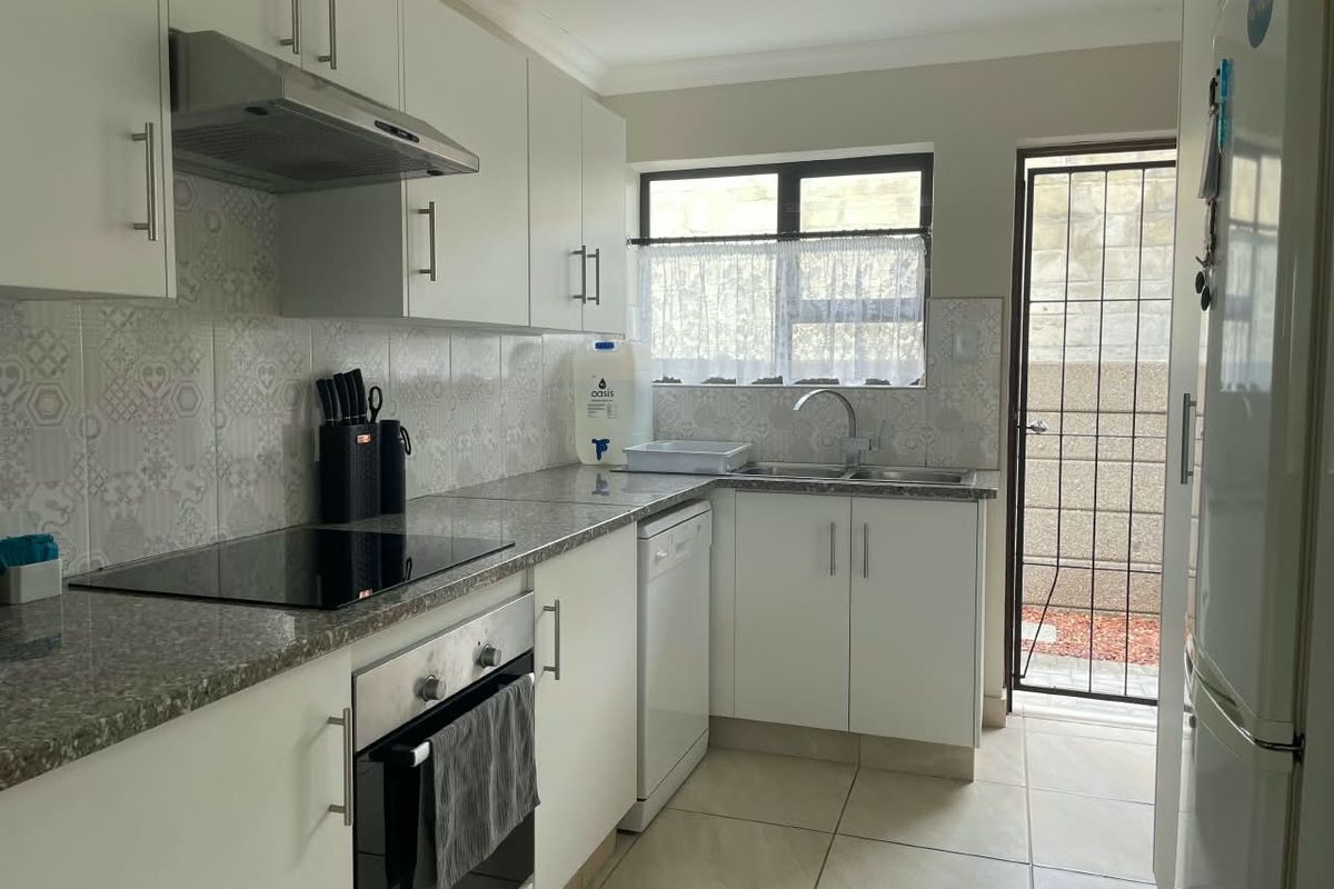 A functional kitchen featuring white cabinetry, granite countertops, integrated appliances, and tiled flooring, with direct access to an exterior area through a security gate.