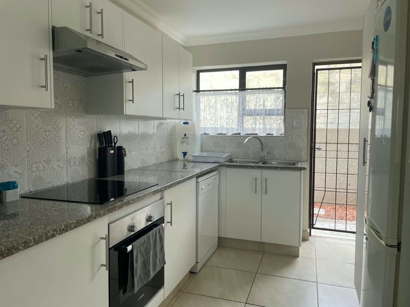A functional kitchen featuring white cabinetry, granite countertops, integrated appliances, and tiled flooring, with direct access to an exterior area through a security gate.