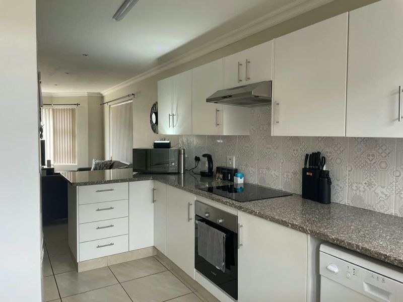 Modern open-plan kitchen featuring white cabinetry, stone-look countertops, patterned tile backsplash, and integrated appliances, flowing into the adjacent living area.